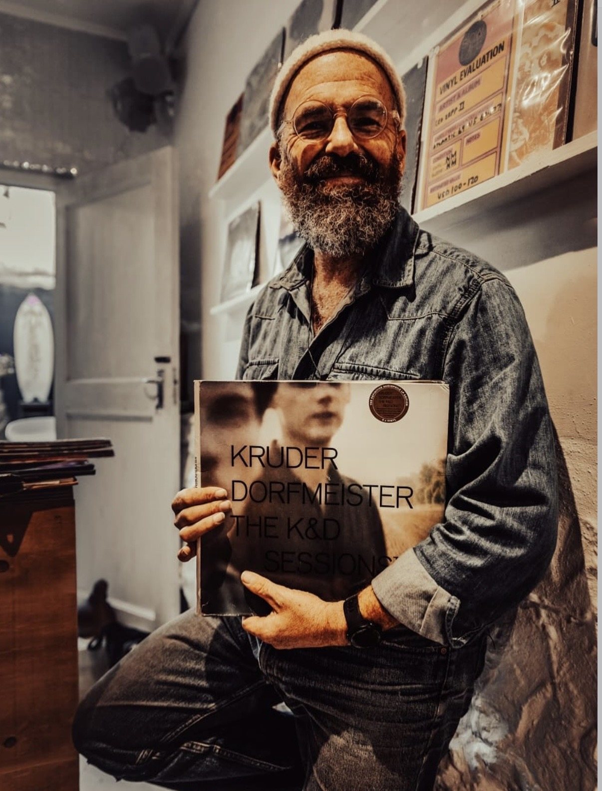 The concierge holds a Kruder and Dorfmeister LP toward the camera inside Slow Life Records
